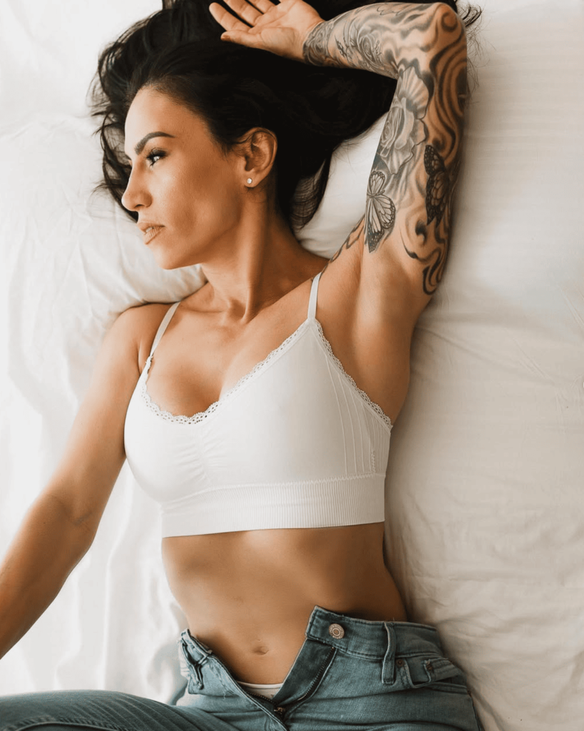 Mulher deitada na cama com top branco e uma calça